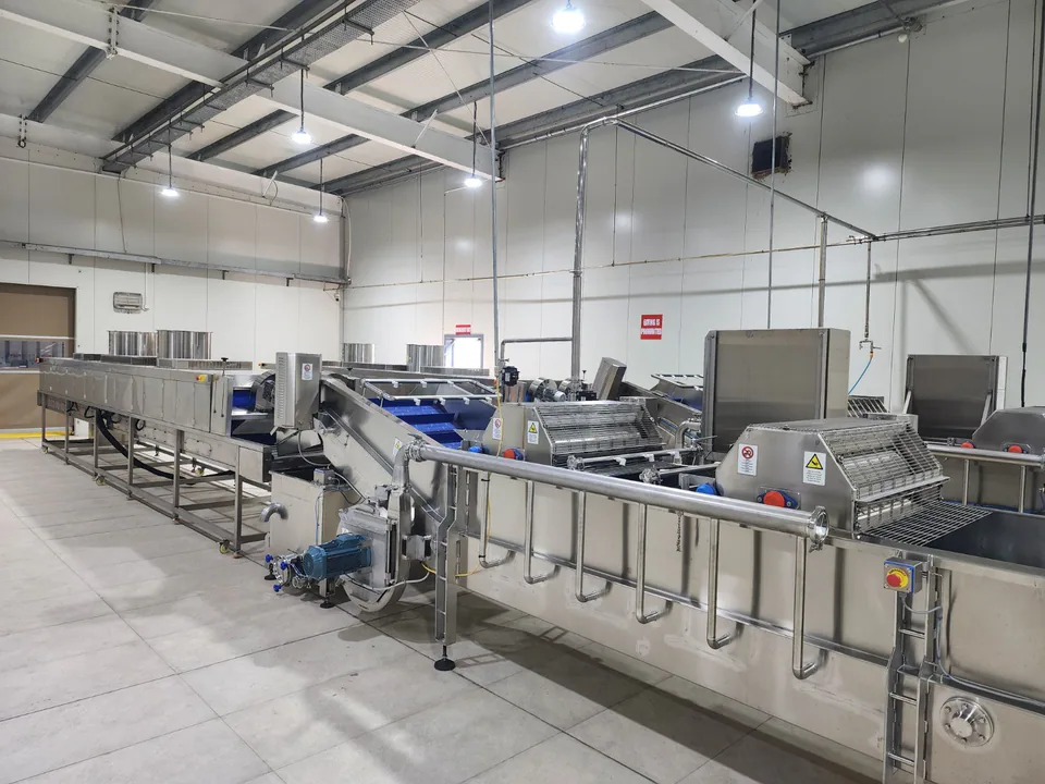 Close view of stainless-steel food-processing equipment and utility pipework inside a production room.